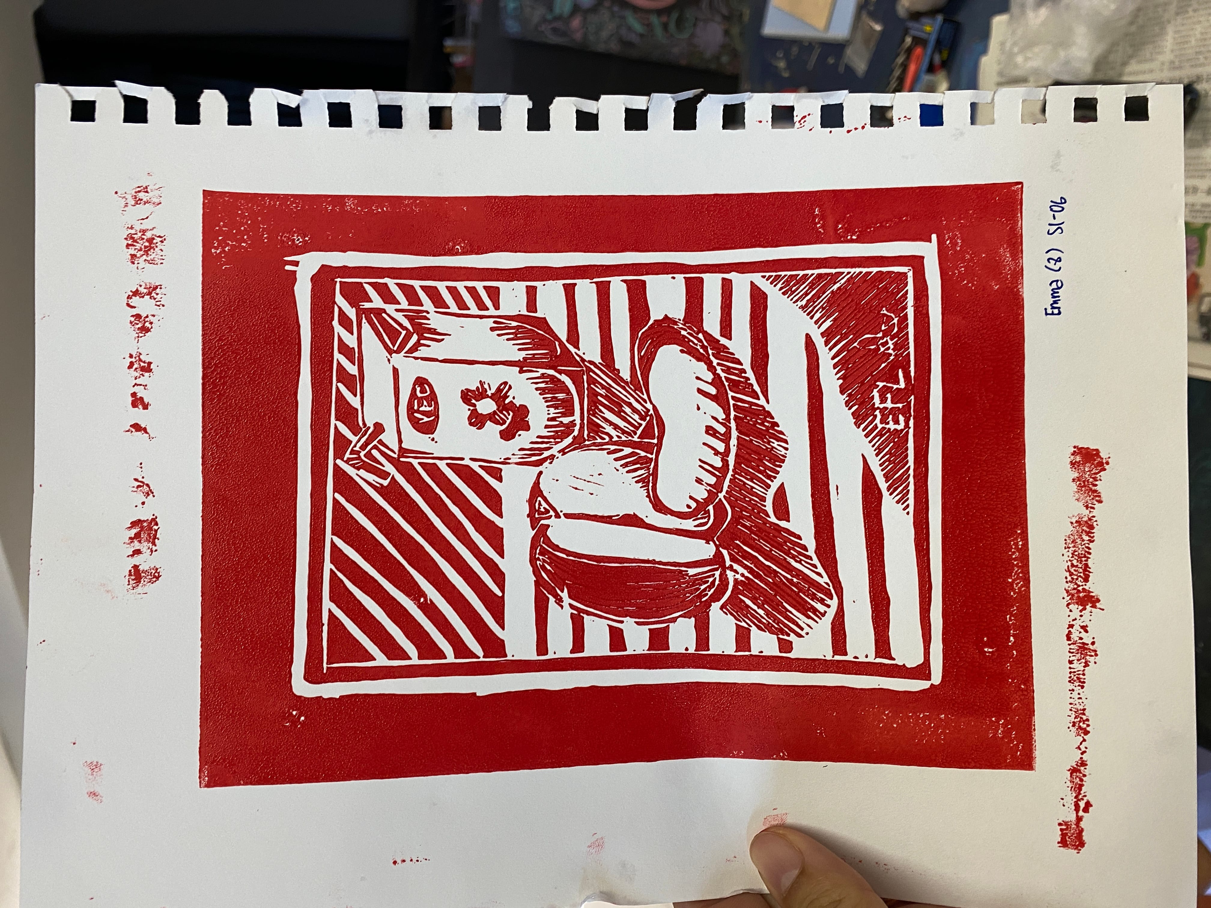 Red linocut print of a table with a cup, spoon, and a carton, framed by striped patterns on white paper.